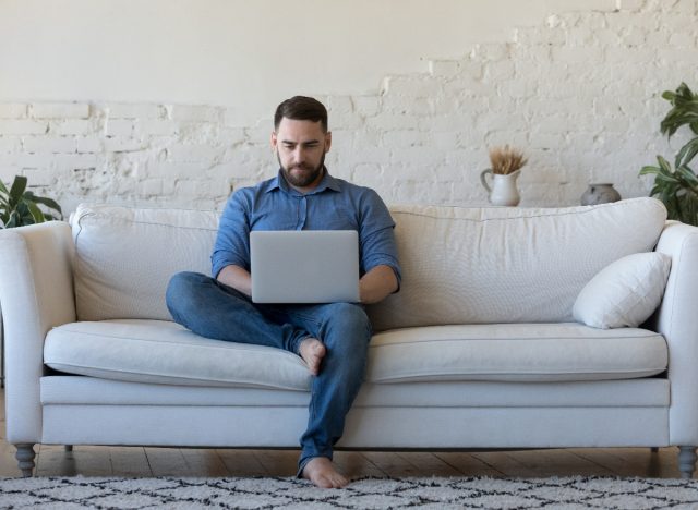 man sitting on sofa typing on laptop