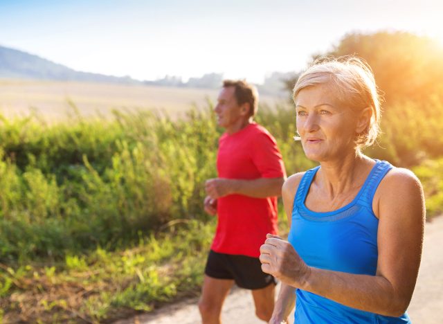 active senior couple walking outdoors in summer on trail, demonstrating benefits of exercise one hour a week