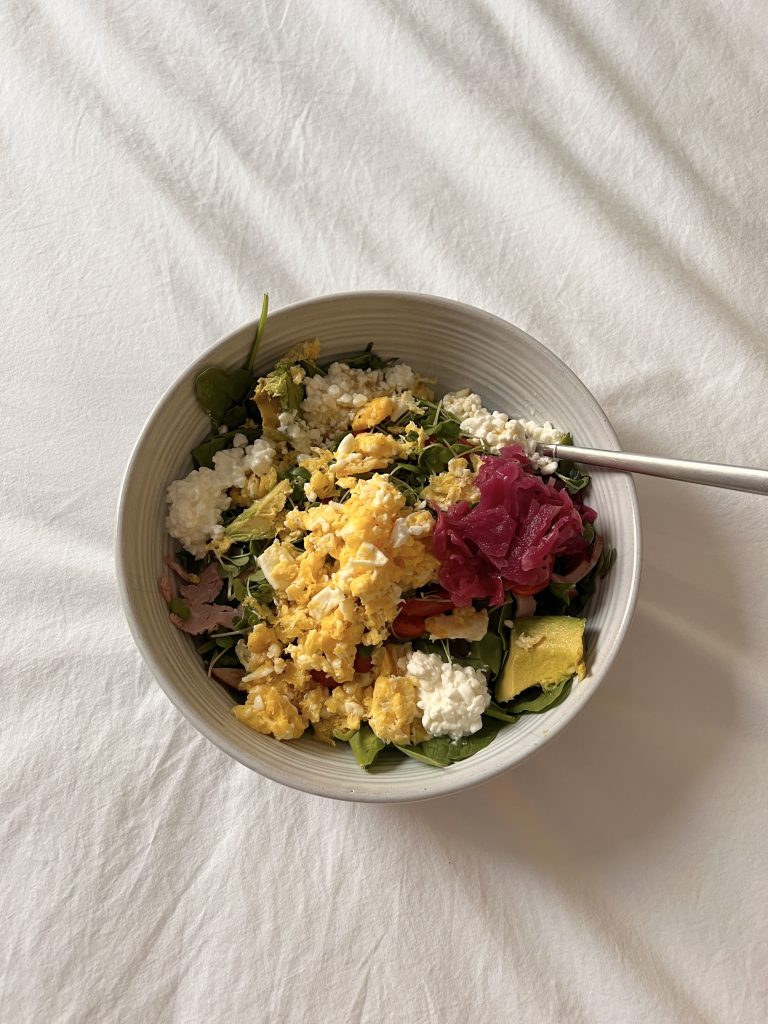 Scrambled eggs, cheese, greens and beetroot sauerkraut in a white bowl.