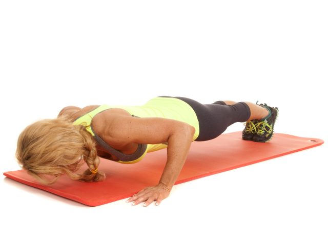woman doing push ups on exercise mat, white background