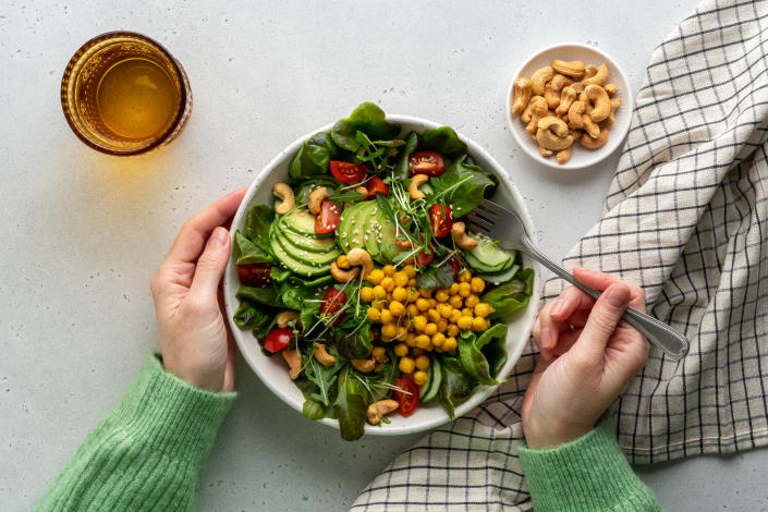 Anonymous woman eating a healthy vegan plant-based salad in a bowl with avocado, cashews, micro greens, pok choy, chickpeas, tomato, lettuce, cucumber, sesame. Flexible fatty acids and dietary fiber