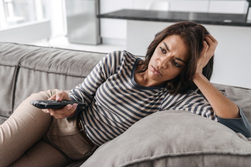A young woman watching TV on the sofa with a disappointed look on her face