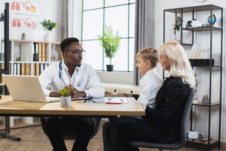 A woman with a baby on her lap talking to a doctor