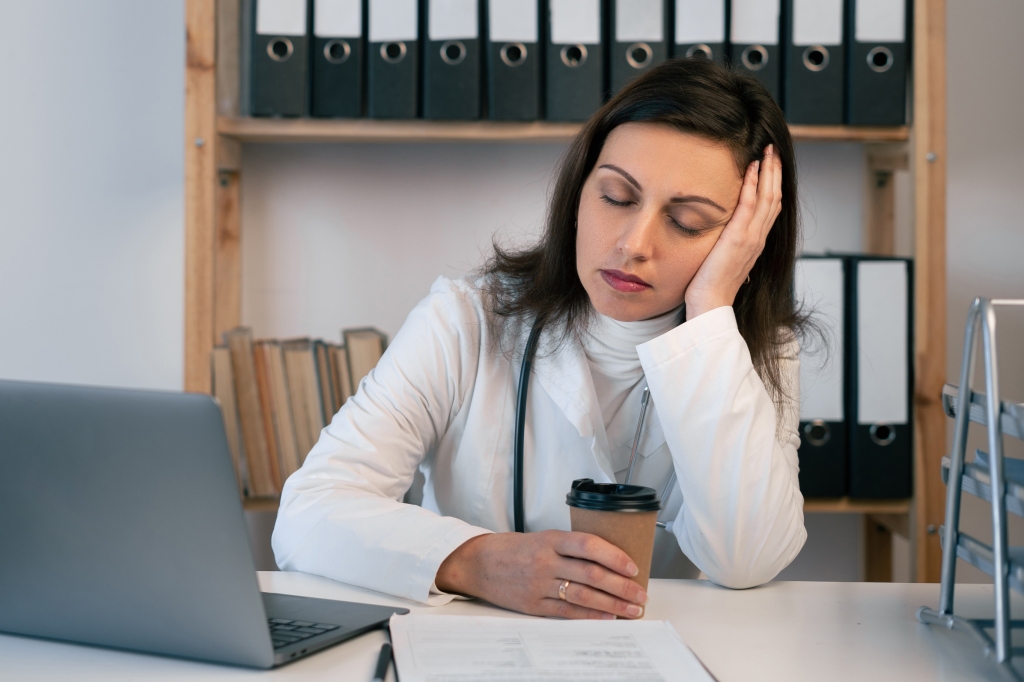 Woman at desk looking exhausted with coffee and laptop.