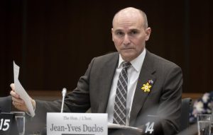 A man in a striped suit and tie seated at a table behind a nameplate with the name of Health Minister Jean-Yves Duclos