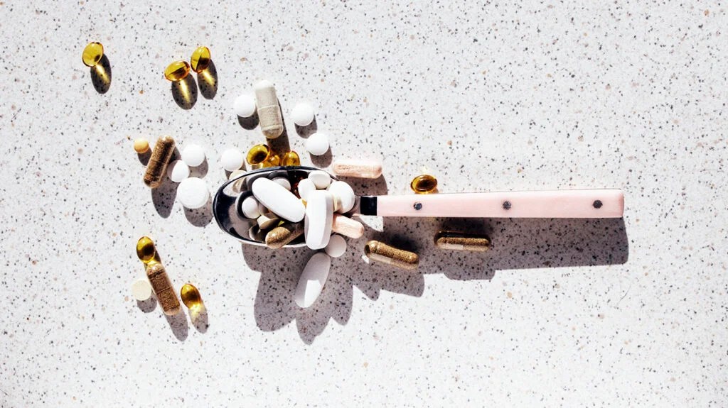 A spoonful of various supplements and probiotics on a gray surface