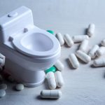 A tiny plastic toilet is surrounded by pills and tablets.