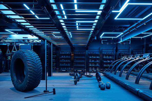 Cool blue light shining on sports equipment in a gymnasium; tire, mallet, treadmill, weights and more pictured