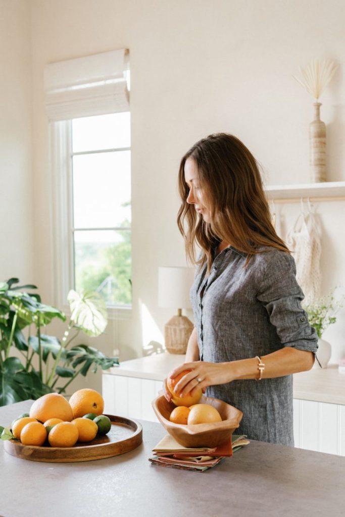 Brunette woman peeling citrus fruits at the kitchen counter.