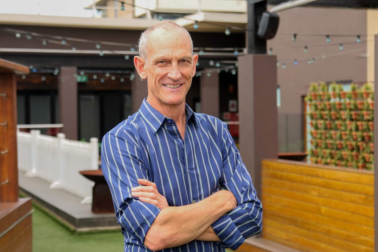 A man in a blue striped shirt is standing with his arms crossed and looking down