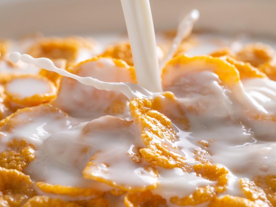 a close up of milk being poured into a bowl of frosted flakes