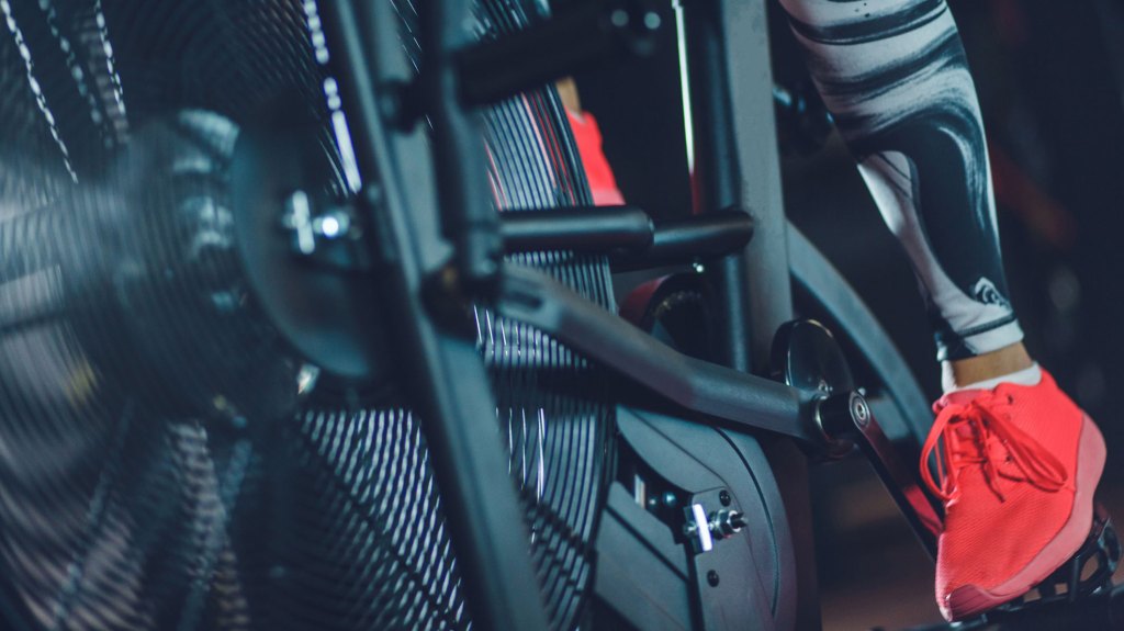 Lower section of unrecognizable female athlete's feet pedaling fixed air bike in gym.
