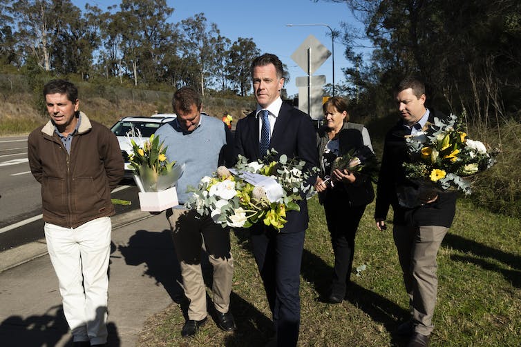 People walking by the roadside carrying bouquets of flowers